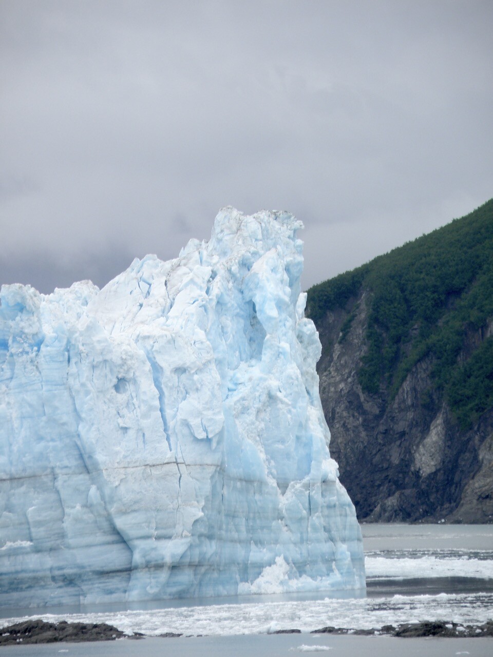 An iceberg, contrasted against a stony cliff.