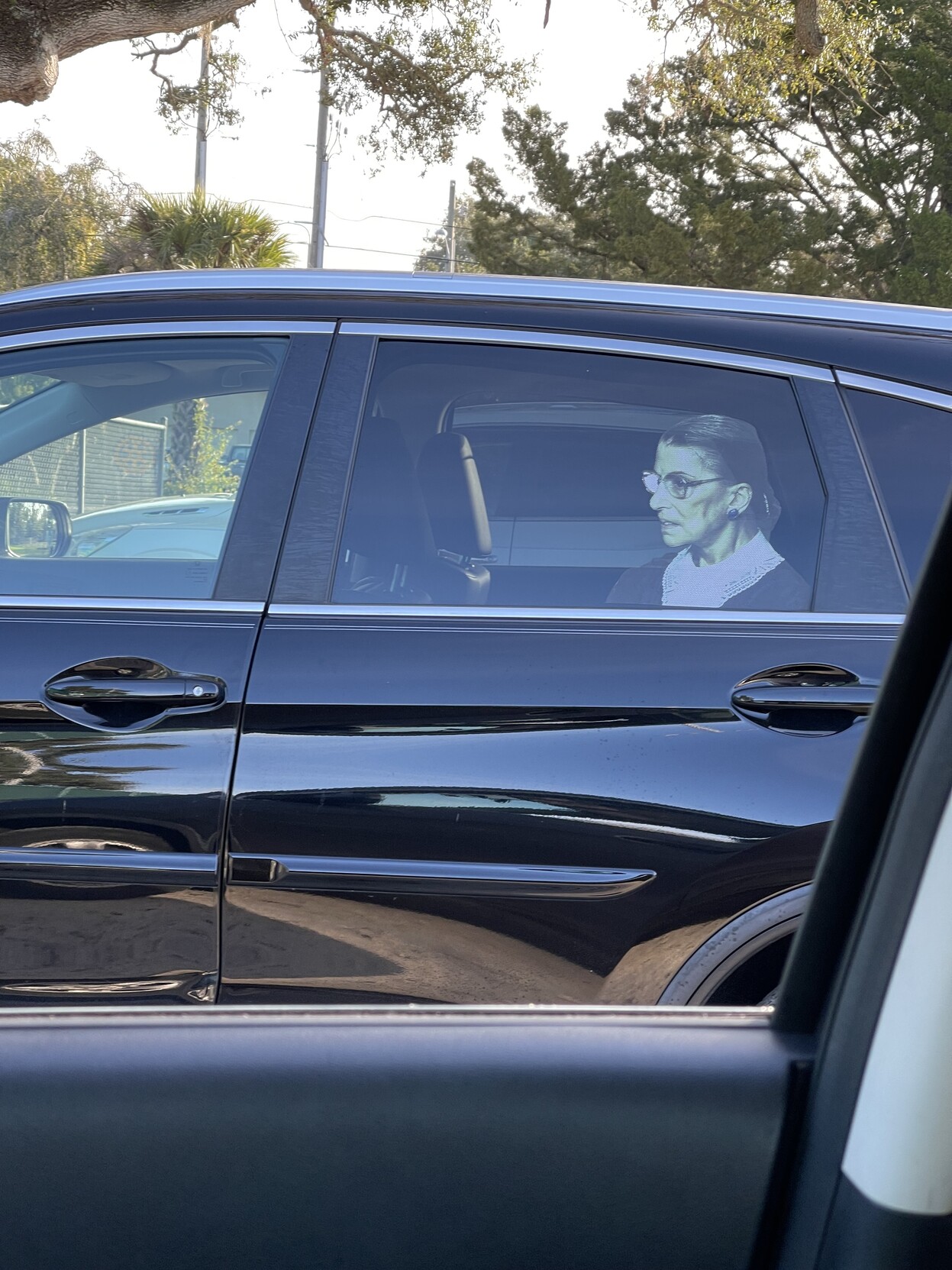 a creepy lifesize image of Ruth Bader Ginsburg through the window of a car in a parking lot.