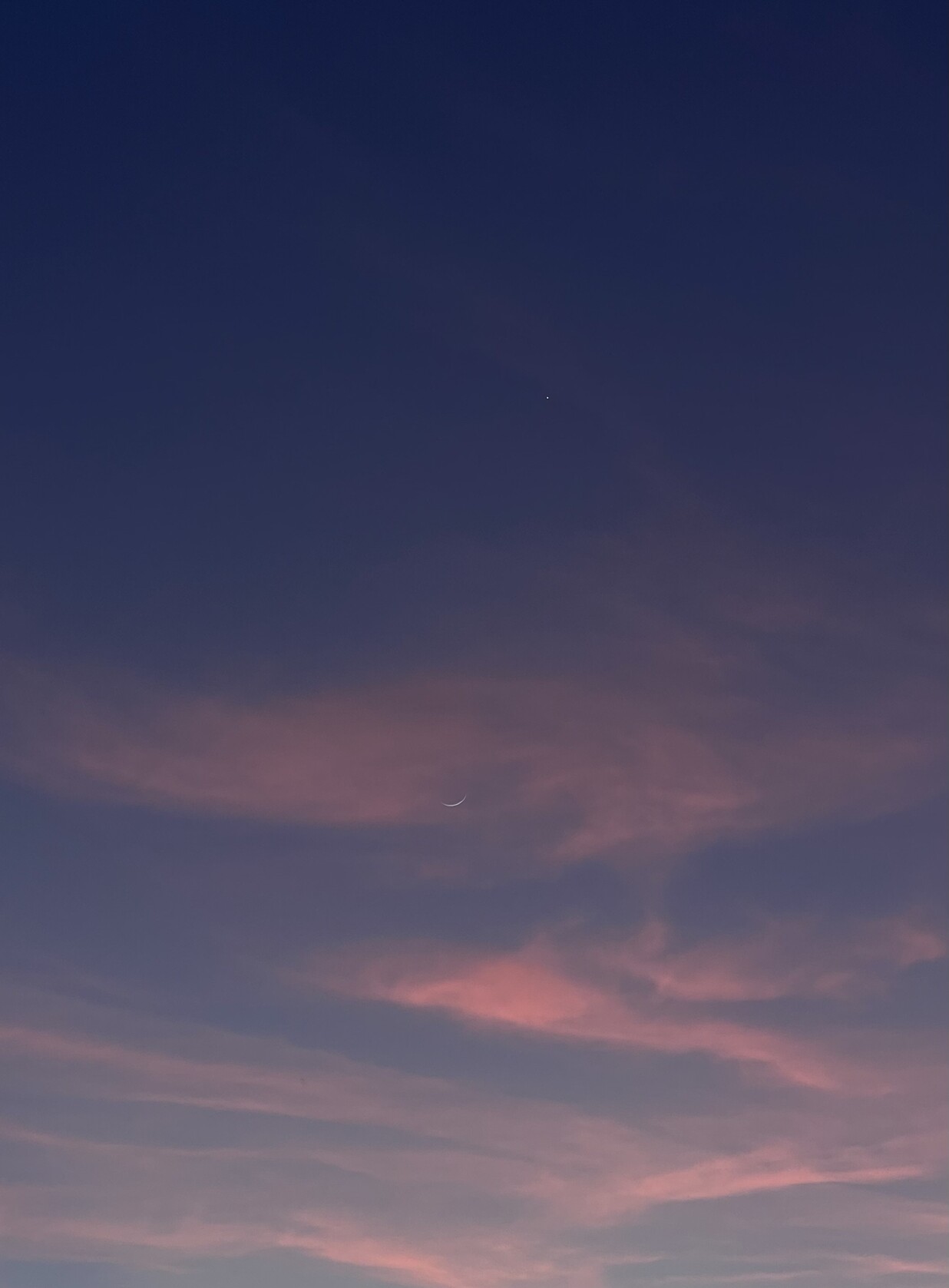 pink clouds superimposed over a new moon, beneath Venus, a glowing white point.